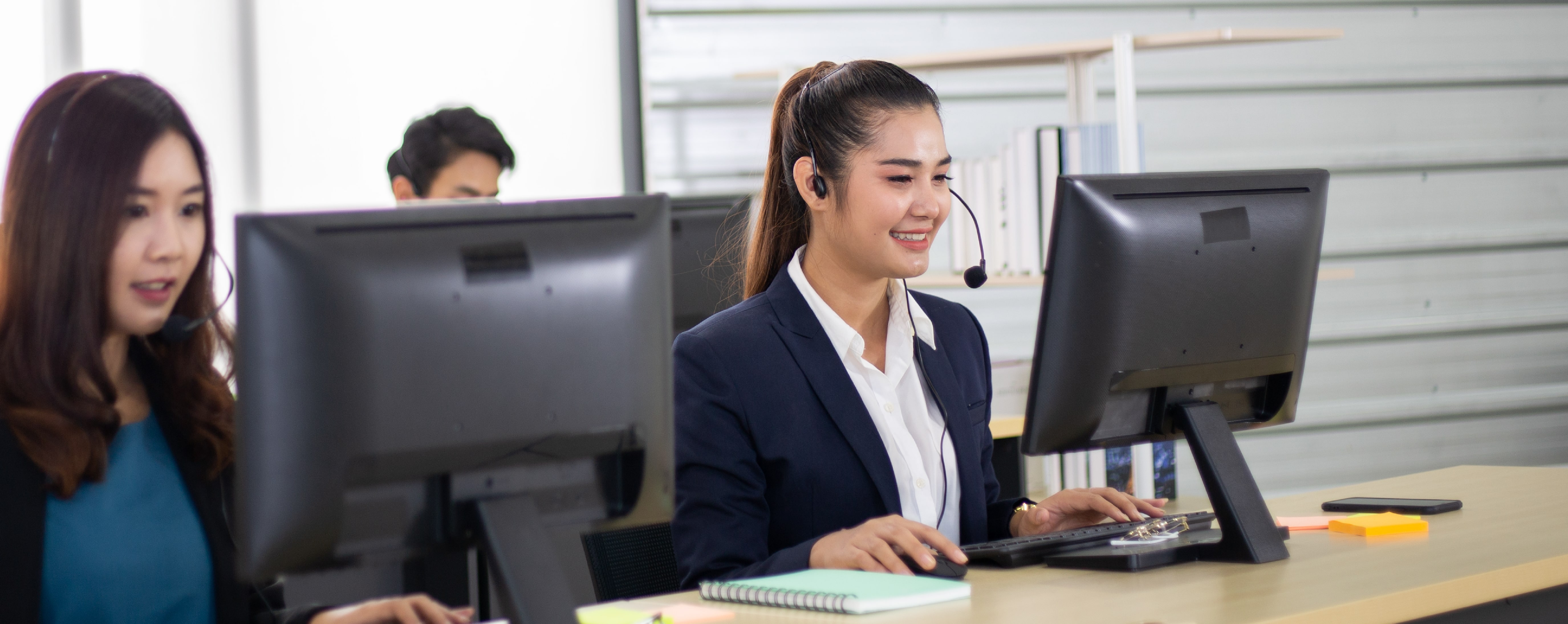 A young woman at her desk answering a call at a contact center.