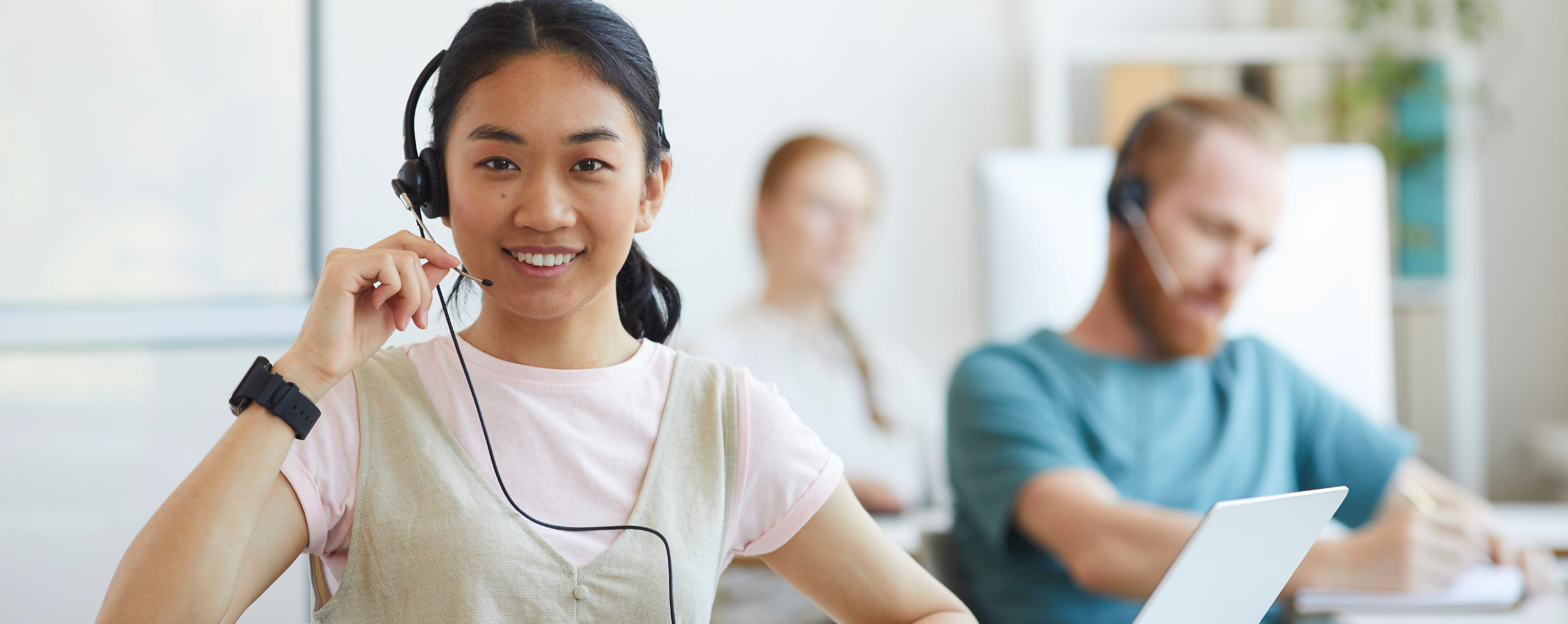 Happy young woman working in a contact center, taking a call while smiling.